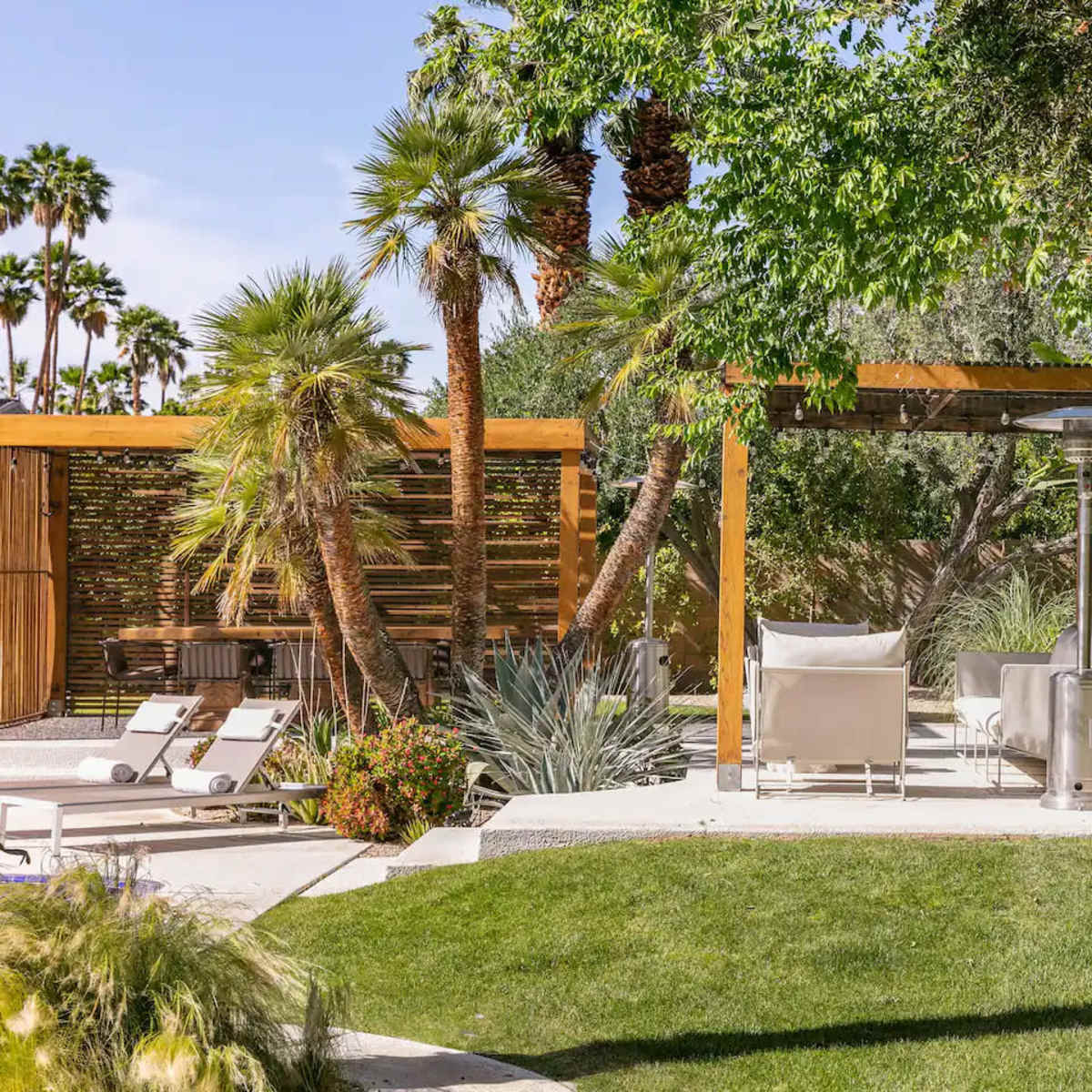 A landscaped outdoor space featuring a seating area with white chairs, surrounded by greenery and palm trees.