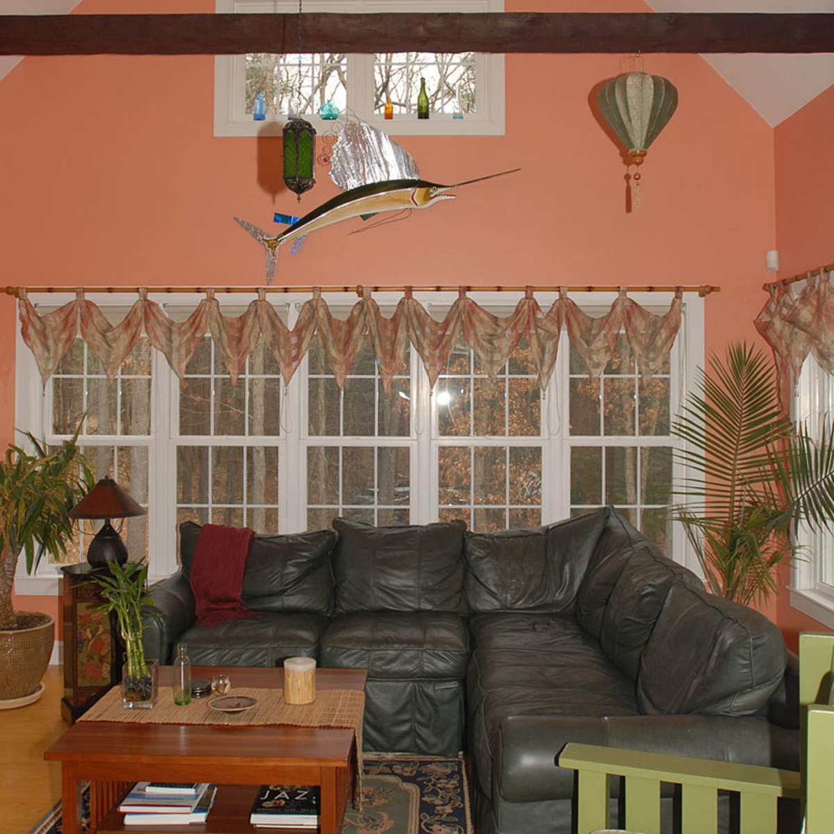 The living room features a large dark green sectional sofa, a wooden coffee table, and multiple windows adorned with patterned curtains.