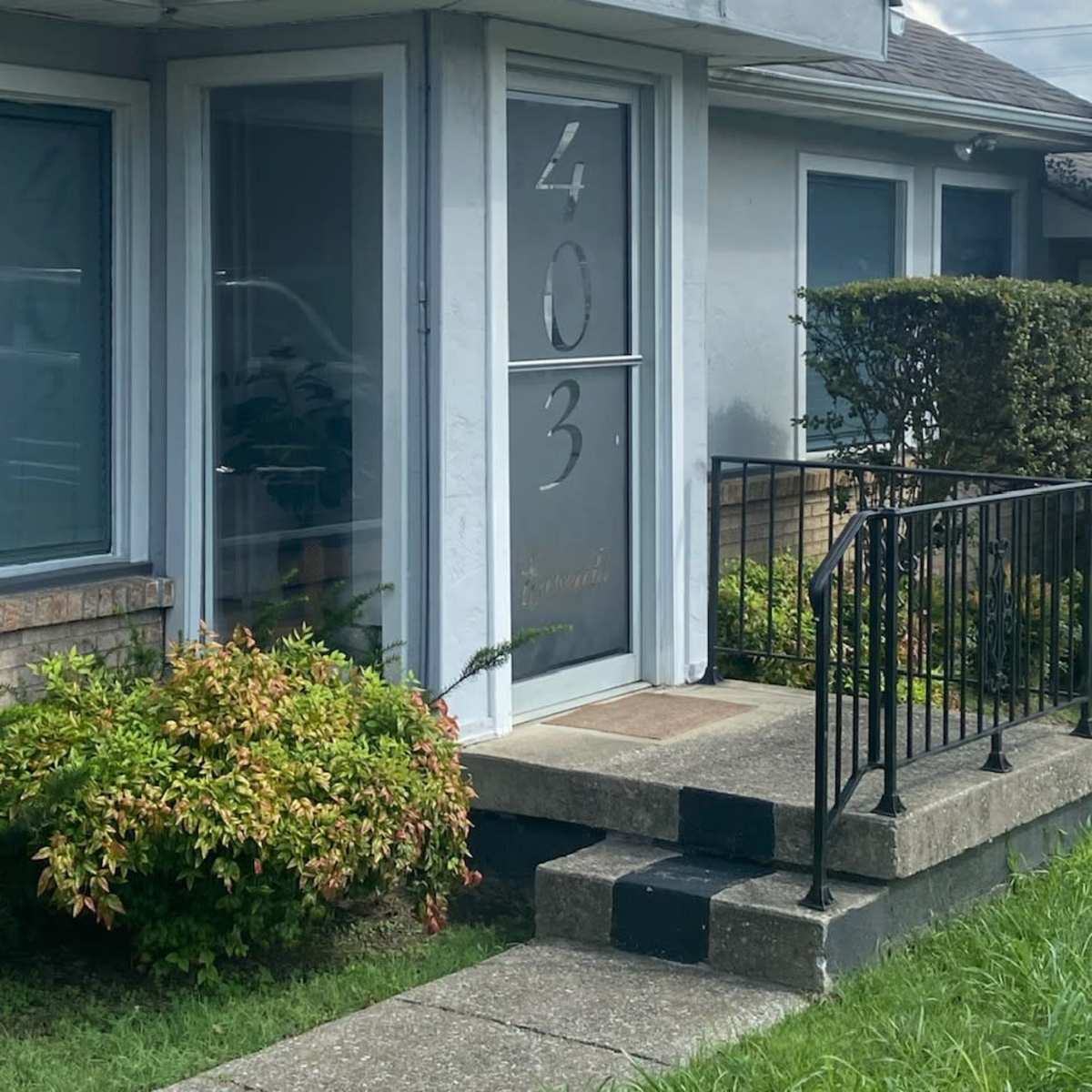 The entrance of a single-story building with a door labeled "403" and a small set of steps leading up to it, surrounded by trimmed bushes.