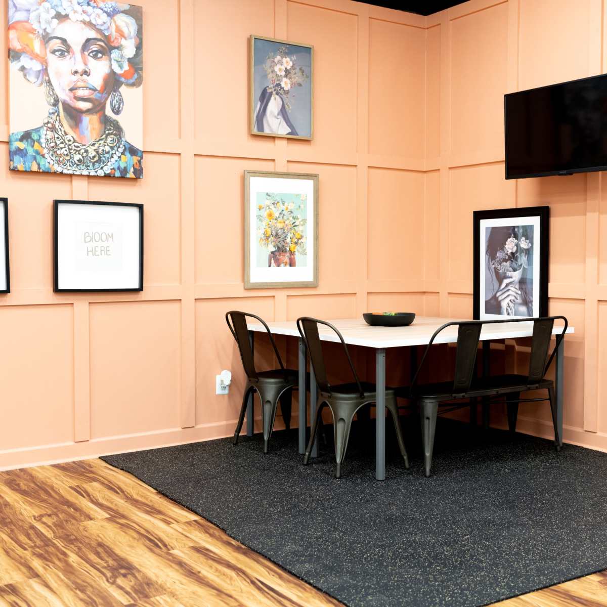 A dining area with a table and chairs, surrounded by peach-colored walls adorned with various framed artworks, and a mounted television in the corner.