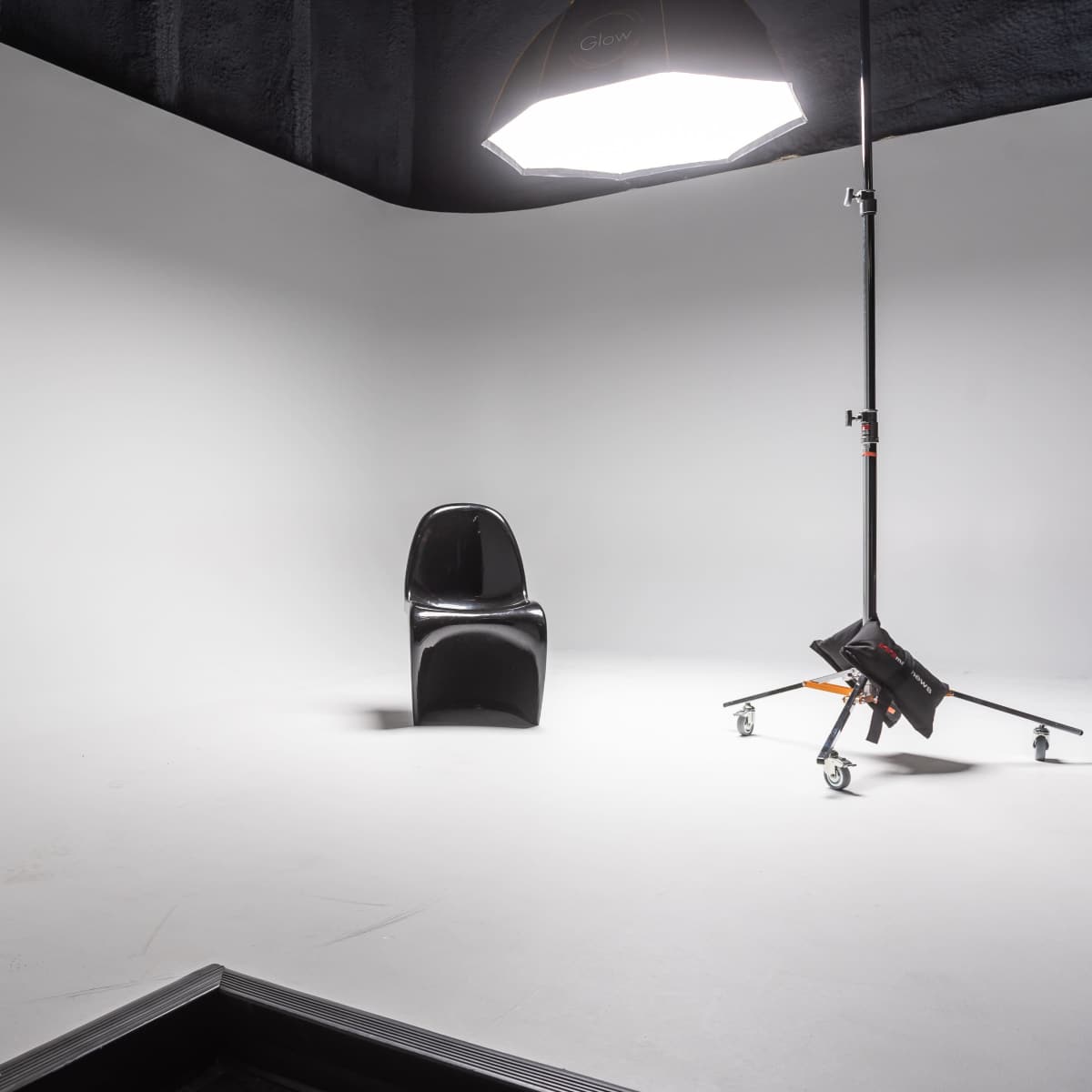 A black chair is positioned in an empty photography studio with a large light source mounted on a stand.