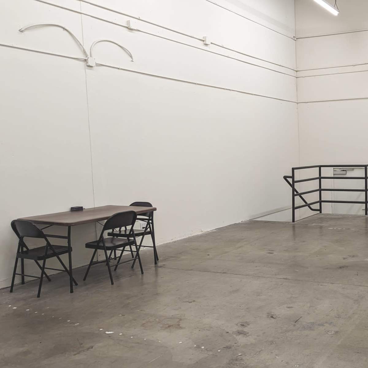 An empty industrial space with a table and chairs on one side and a large rolling garage door on the opposite side.