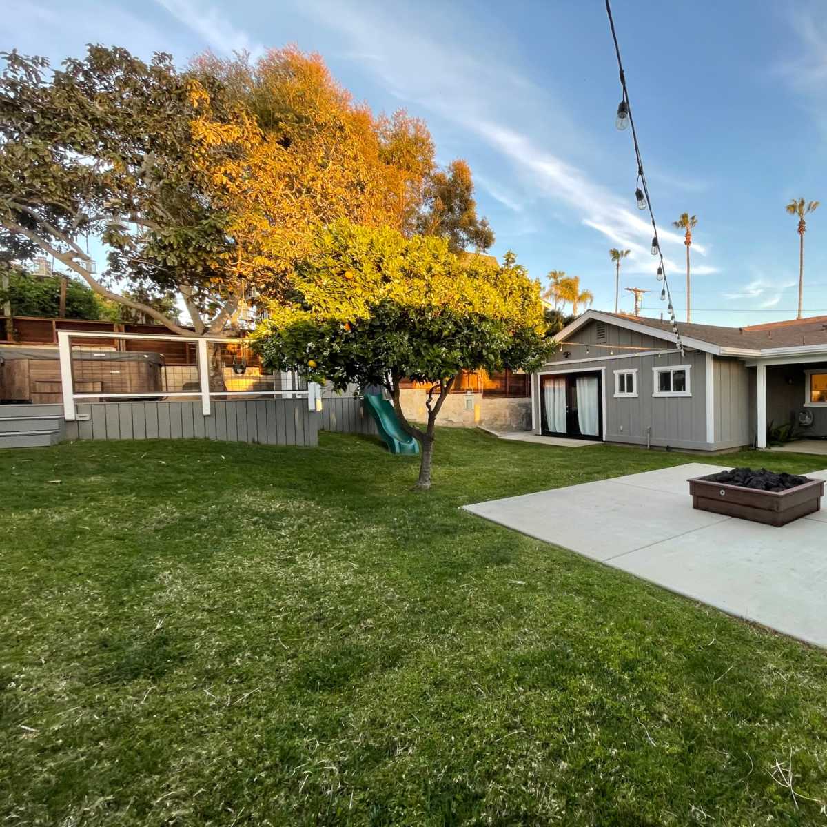 A backyard with a grassy area, a wooden play structure, a small tree, and a house featuring sliding glass doors.
