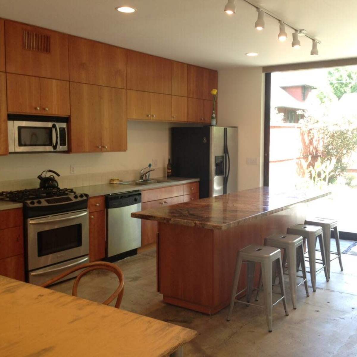 The kitchen features wooden cabinets, stainless steel appliances, a marble-topped island, and large sliding glass doors leading to an outdoor area.