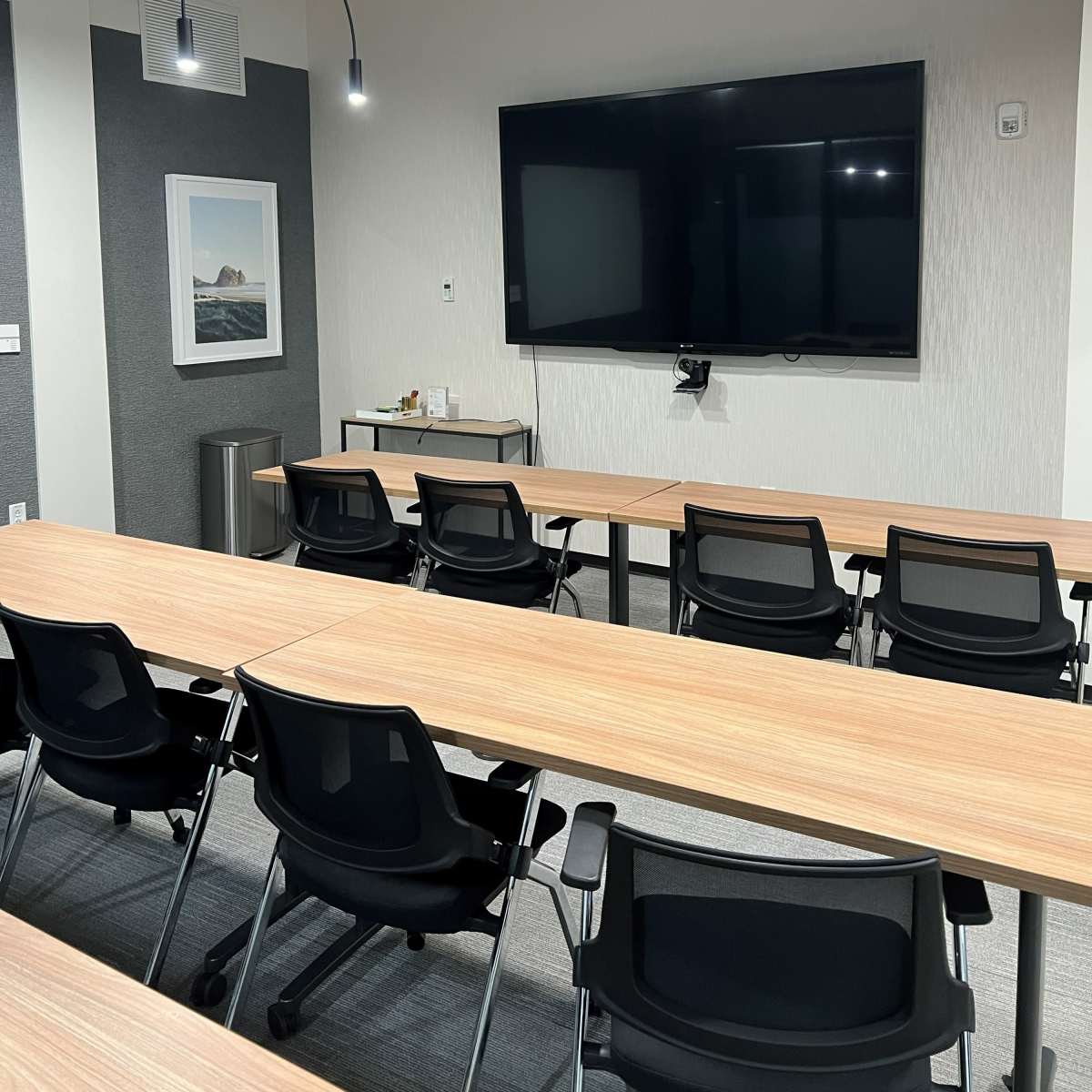 A modern conference room features a large screen, wooden tables, and black chairs arranged for meetings.