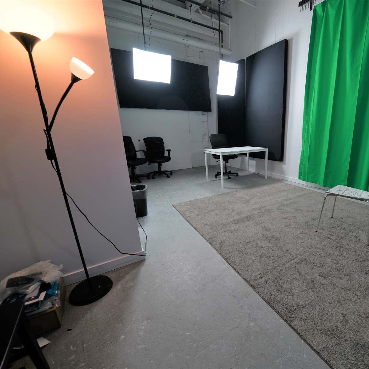 A studio space features a green backdrop, a chair, a table, and lighting equipment.