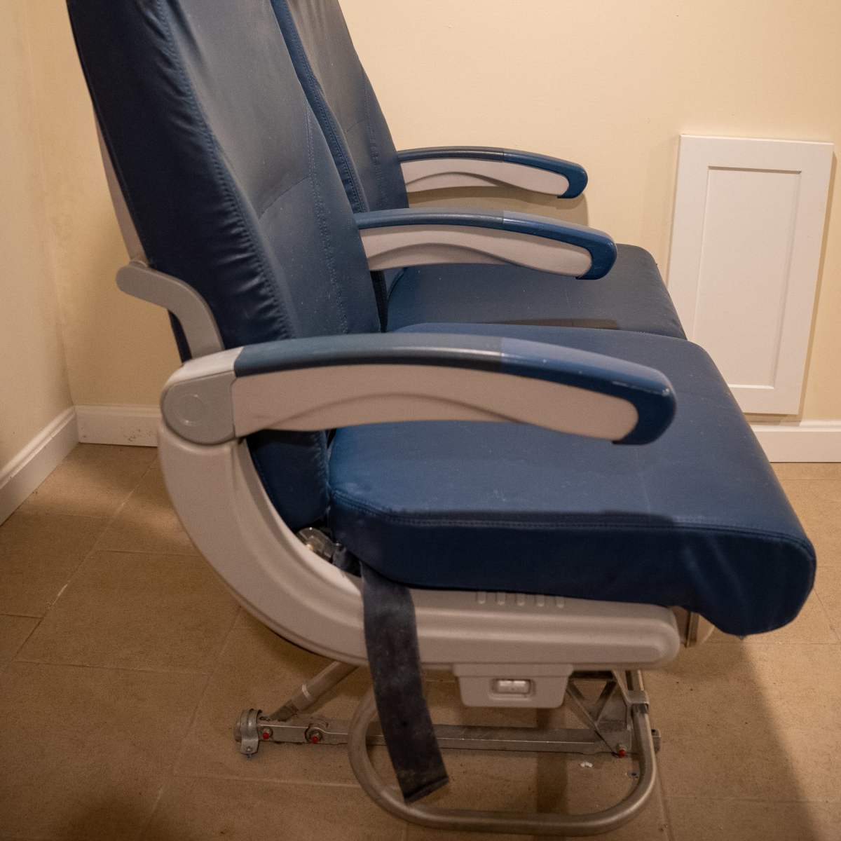 Two blue airplane seats are positioned side by side, accompanied by a window display showing a sky view.