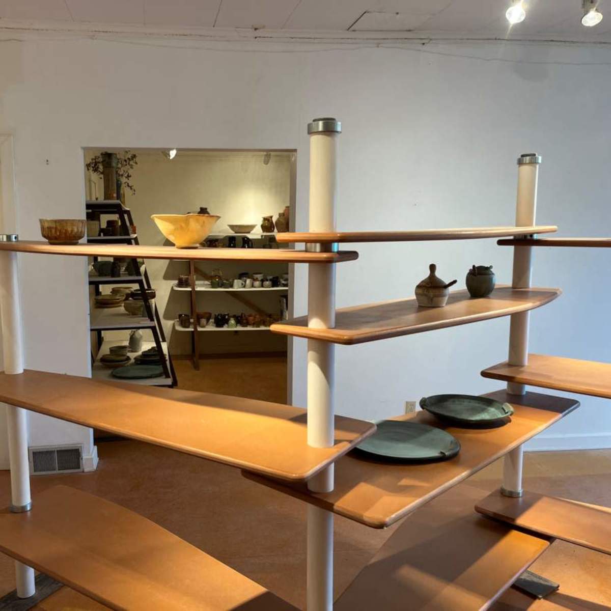 A modern display shelving unit showcases various pottery and dishes in a well-lit room.