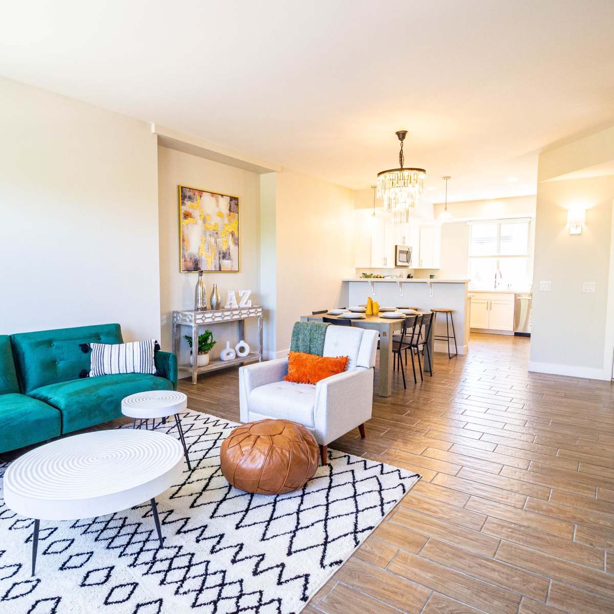 A spacious living area features a green couch, a white coffee table, and a decorative area rug, leading to a kitchen and dining space in the background.