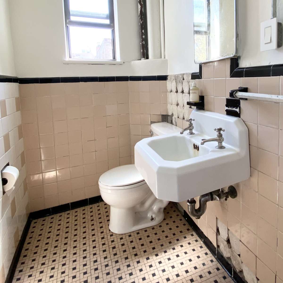 A small, tiled bathroom features a wall-mounted sink and a toilet against a patterned floor.