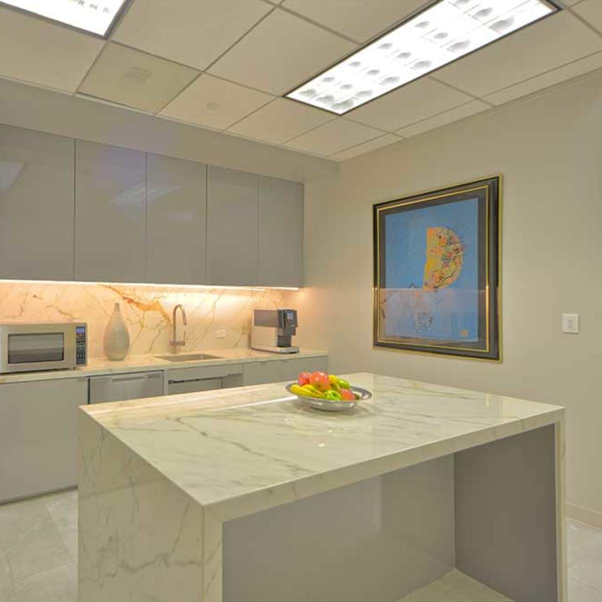 A modern kitchen featuring gray cabinets, a marble countertop, and stainless steel appliances, including a refrigerator and microwave.
