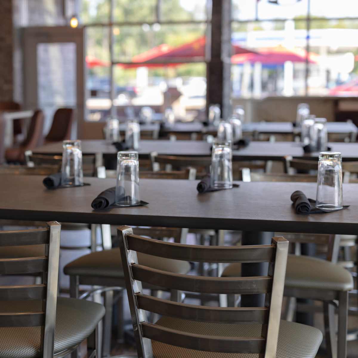 A dining area features metal chairs and a long table set with water glasses and napkins.