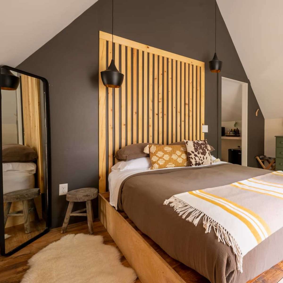 A cozy bedroom featuring a bed with a wooden headboard, a patterned throw, and a large mirror against the wall.