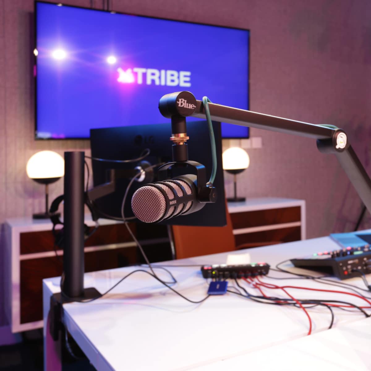 A modern podcasting studio featuring a microphone on an adjustable arm, a digital mixing console, and a large screen displaying the word "TRIBE."