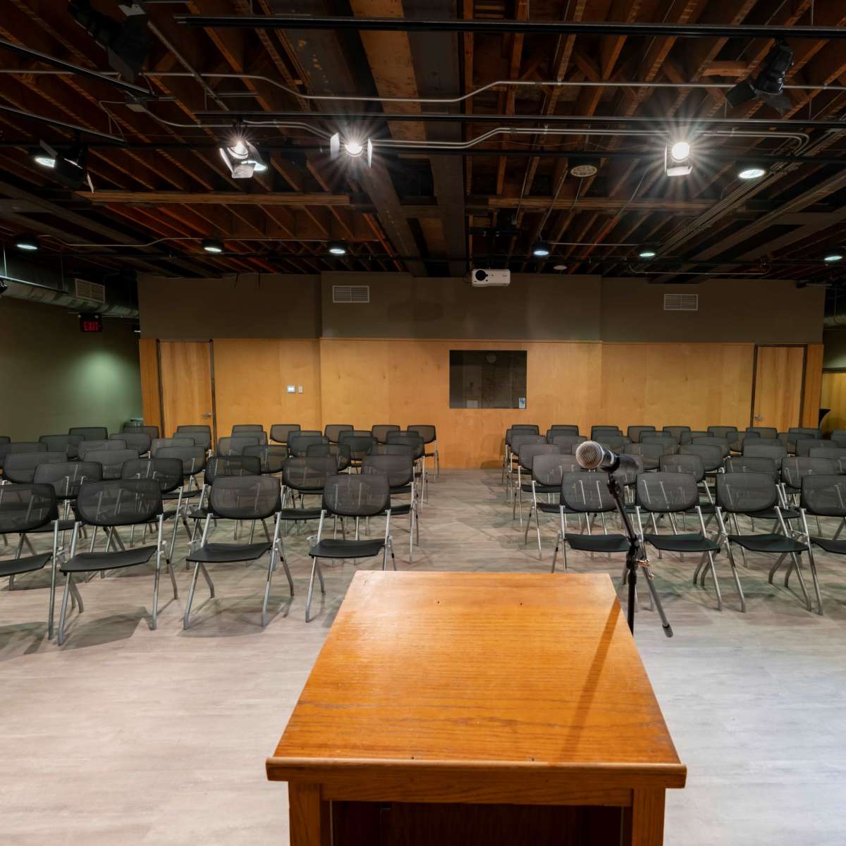 A semi-empty auditorium with rows of metal folding chairs facing a wooden podium under dim ceiling lights.