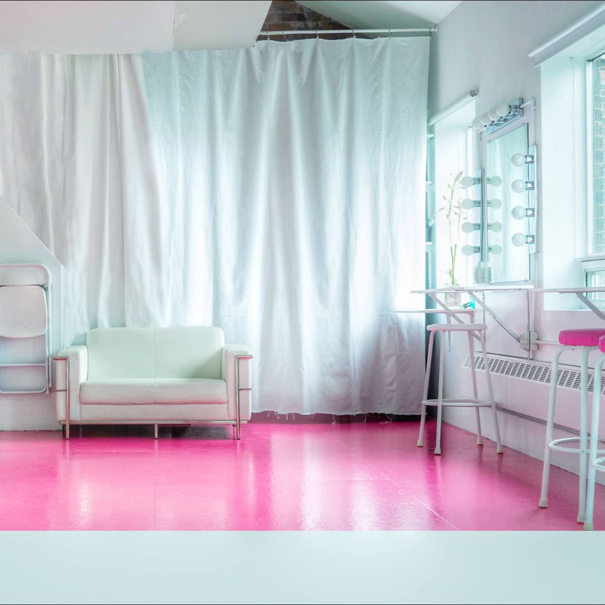 A modern room with pink flooring, a light green couch, and a bar area with stools.