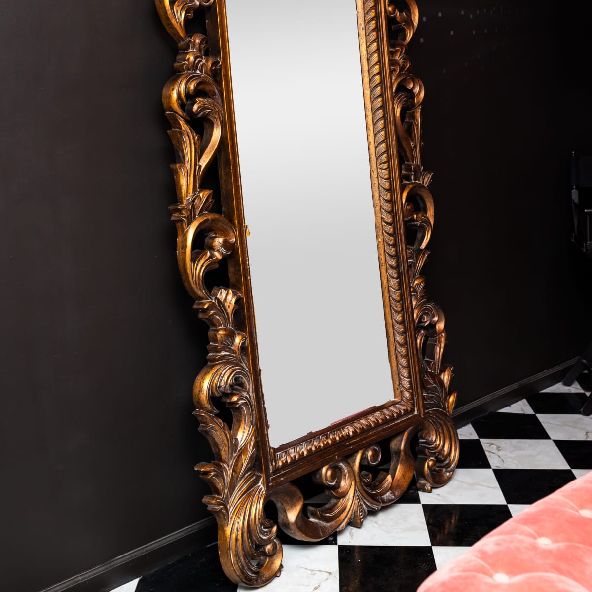 A large, ornate mirror with a decorative golden frame is positioned against a black wall, reflecting its surroundings.