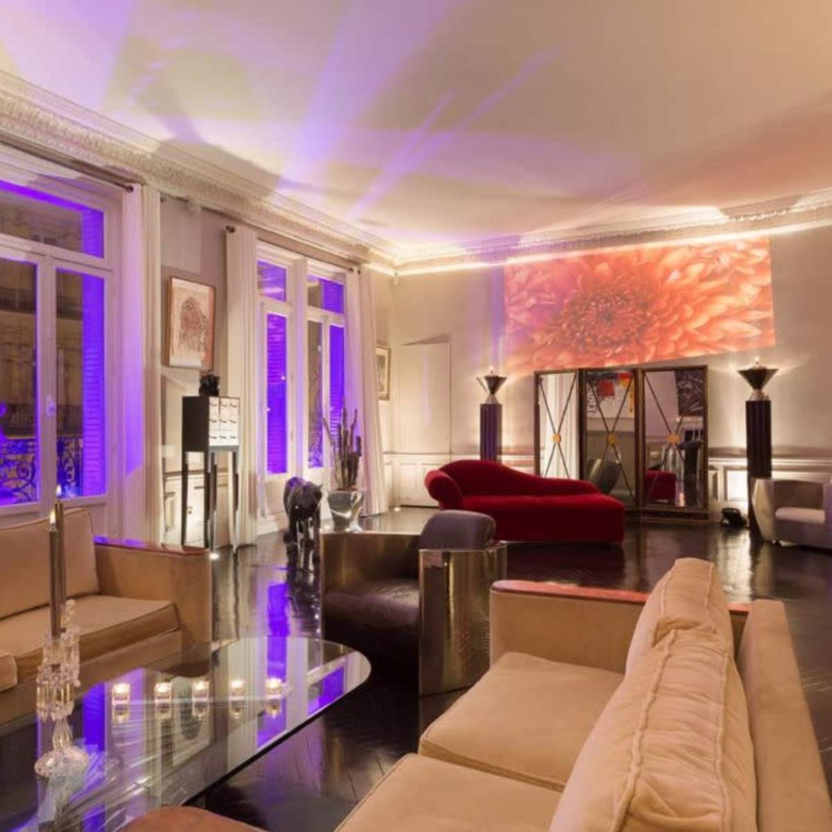 A spacious living room featuring modern furniture, large windows, and purple accent lighting.