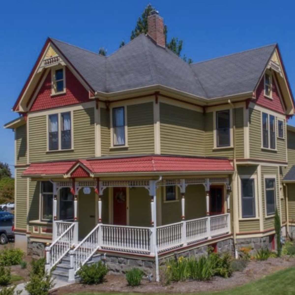 A large, two-story Victorian-style house with a wraparound porch and colorful trim sits in a landscaped yard.