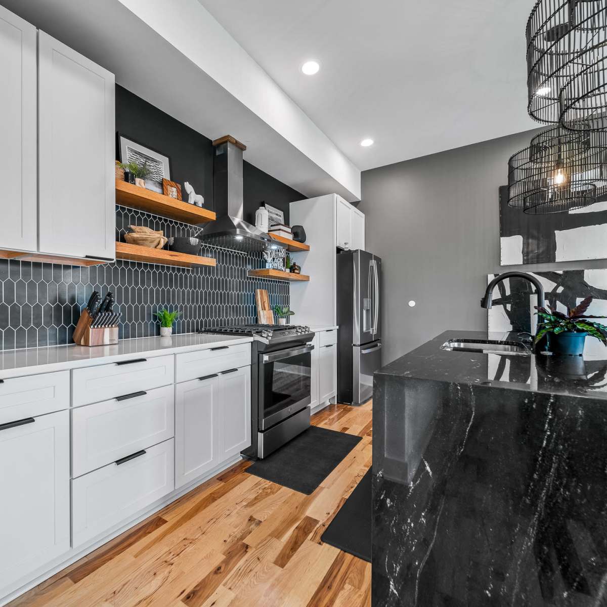 A modern kitchen features white cabinetry, a black stone island, and hexagonal tile backsplash.
