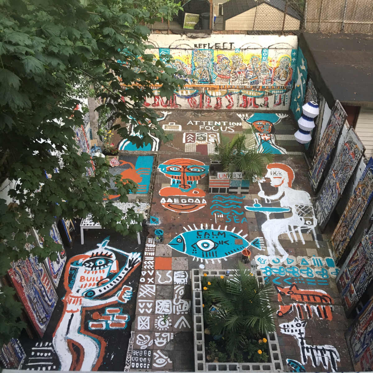 A vibrant outdoor space covered with colorful street art and murals, surrounded by greenery and buildings.