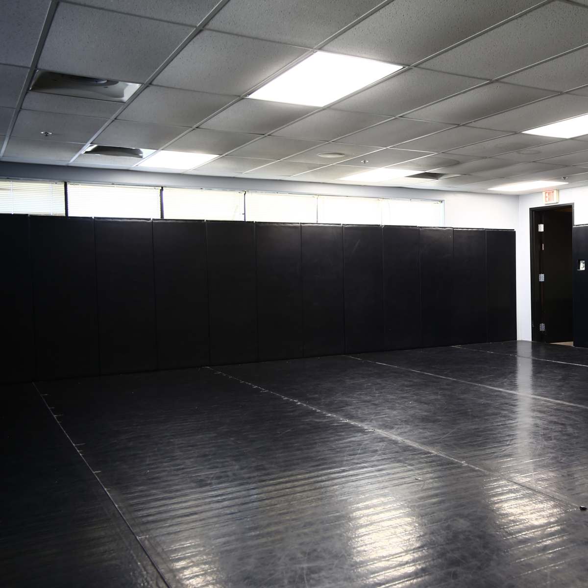 An empty martial arts studio with black padded walls and a rubber flooring surface.