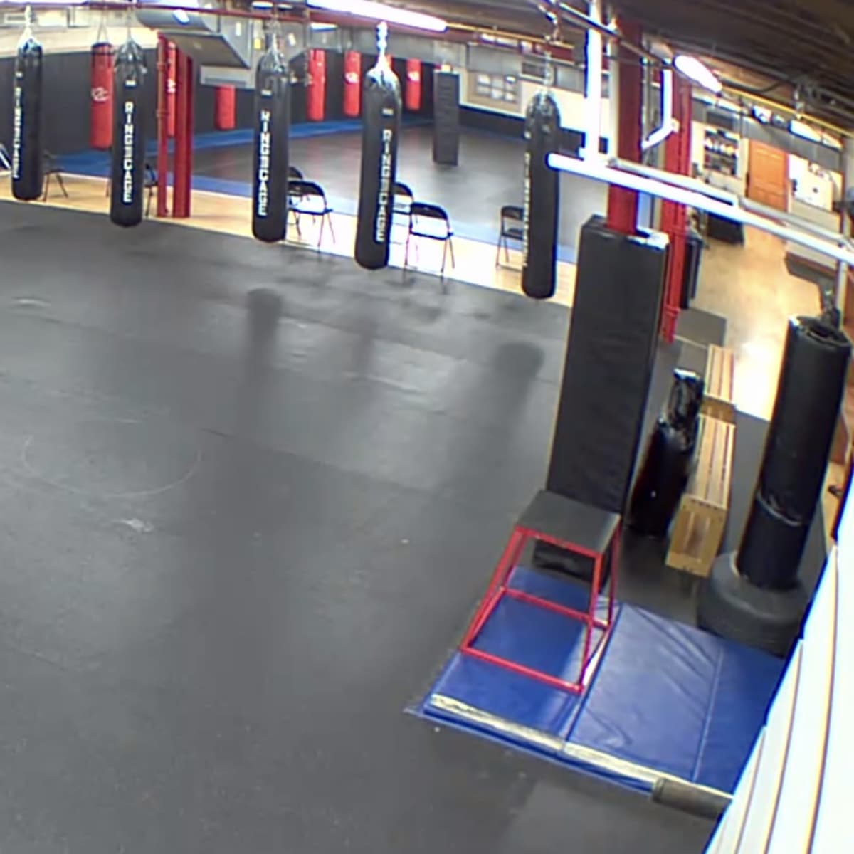 A spacious training area with various exercise equipment, including weights, punching bags, and mats, in a gym setting.
