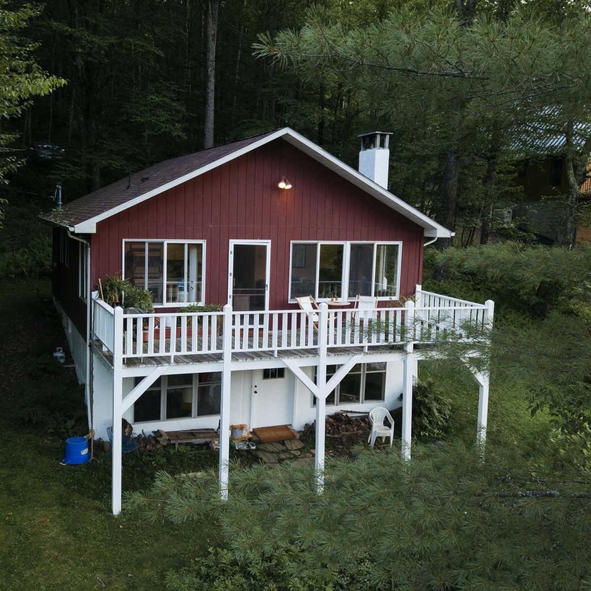 A two-story red house with a white balcony is surrounded by dense trees and greenery.