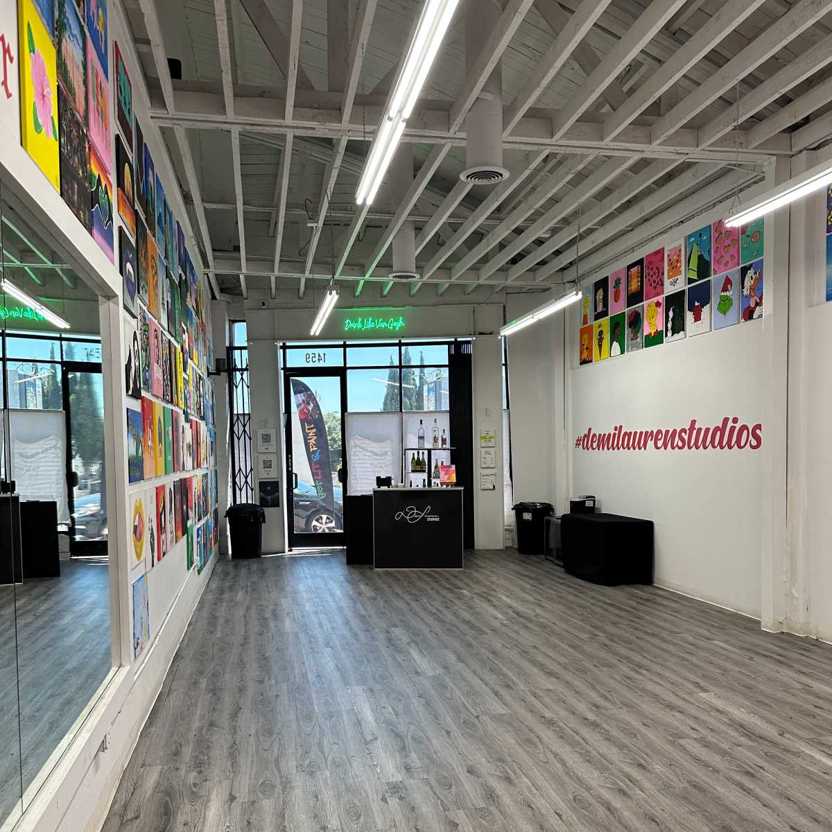 A spacious art studio with a mirrored wall, colorful artworks displayed on one side, and a reception area featuring a desk and signage.
