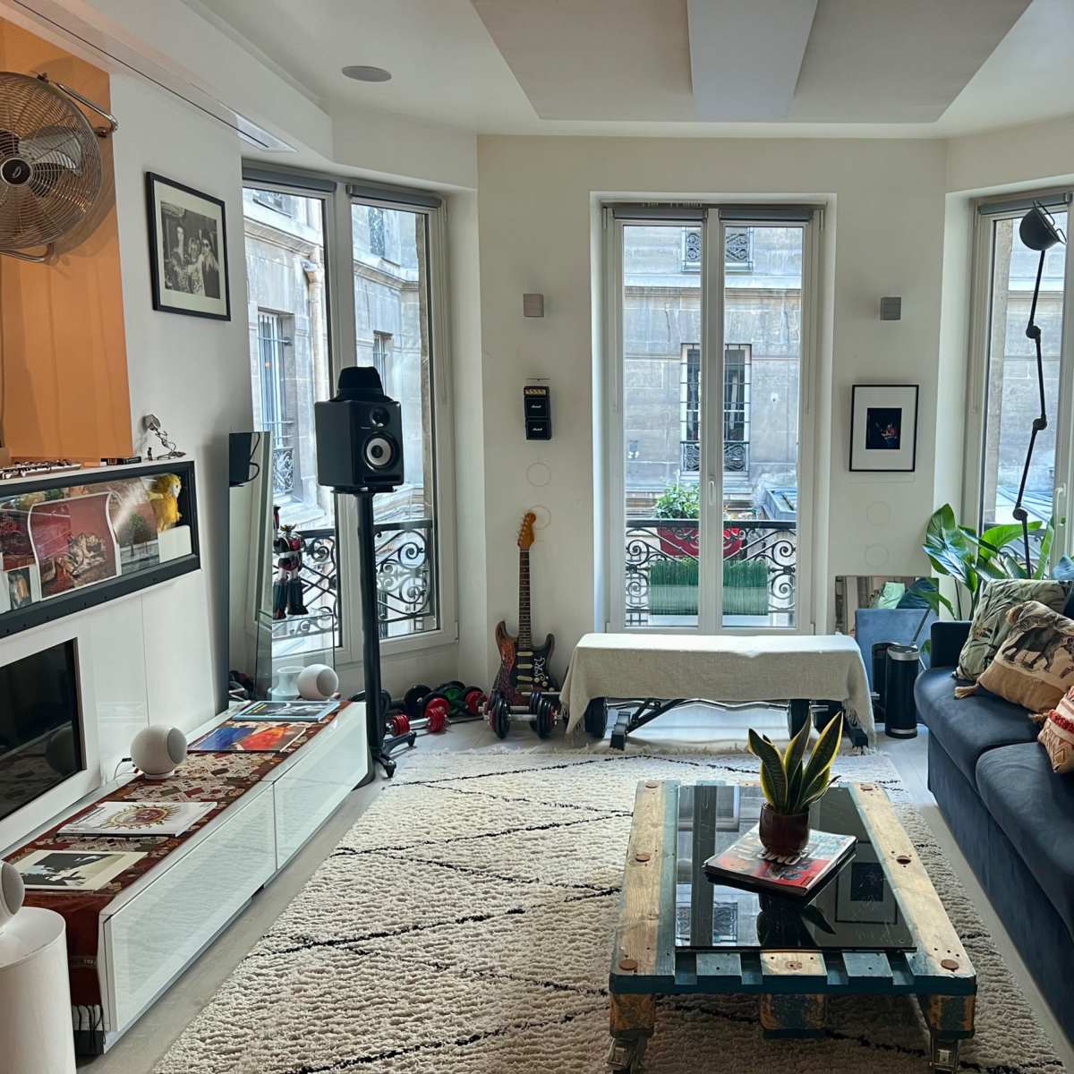 The living room features a couch, a coffee table, a guitar, and large windows that overlook an external balcony.