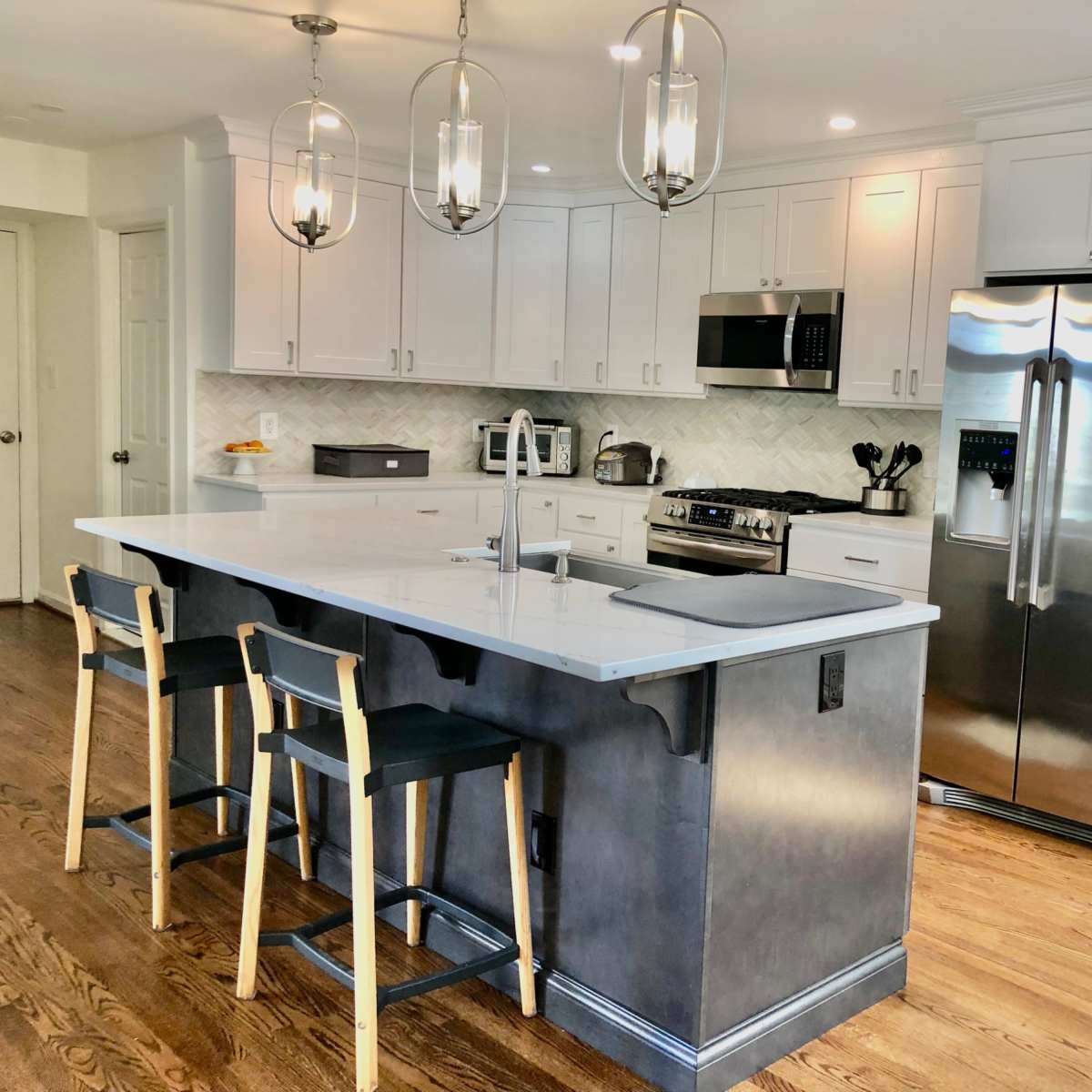 A modern kitchen features white cabinetry, stainless steel appliances, a gray island with seating, and wooden flooring.