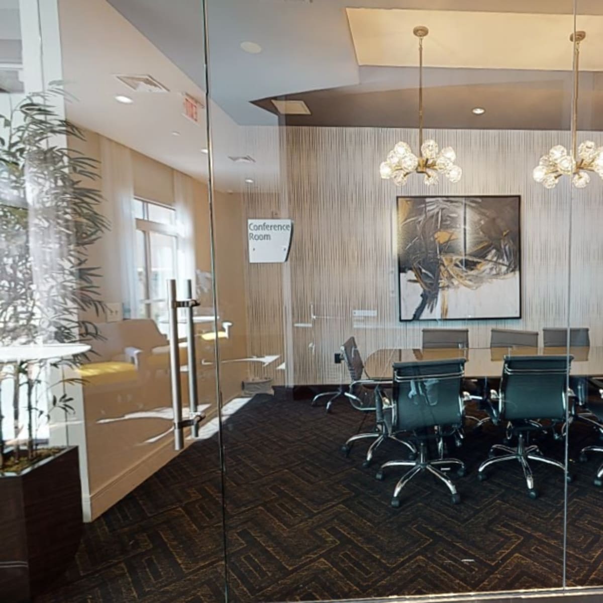 A modern conference room with a large table and black chairs, enclosed by glass walls and featuring decorative elements on the walls.