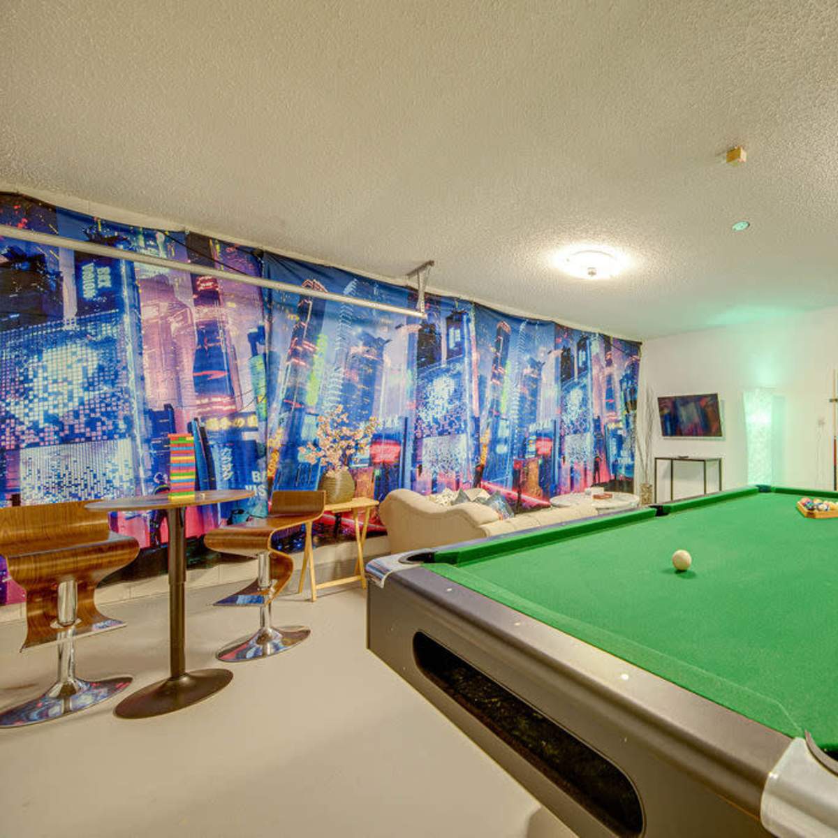 A pool table is positioned in a room with colorful wall murals, modern seating, and a television.