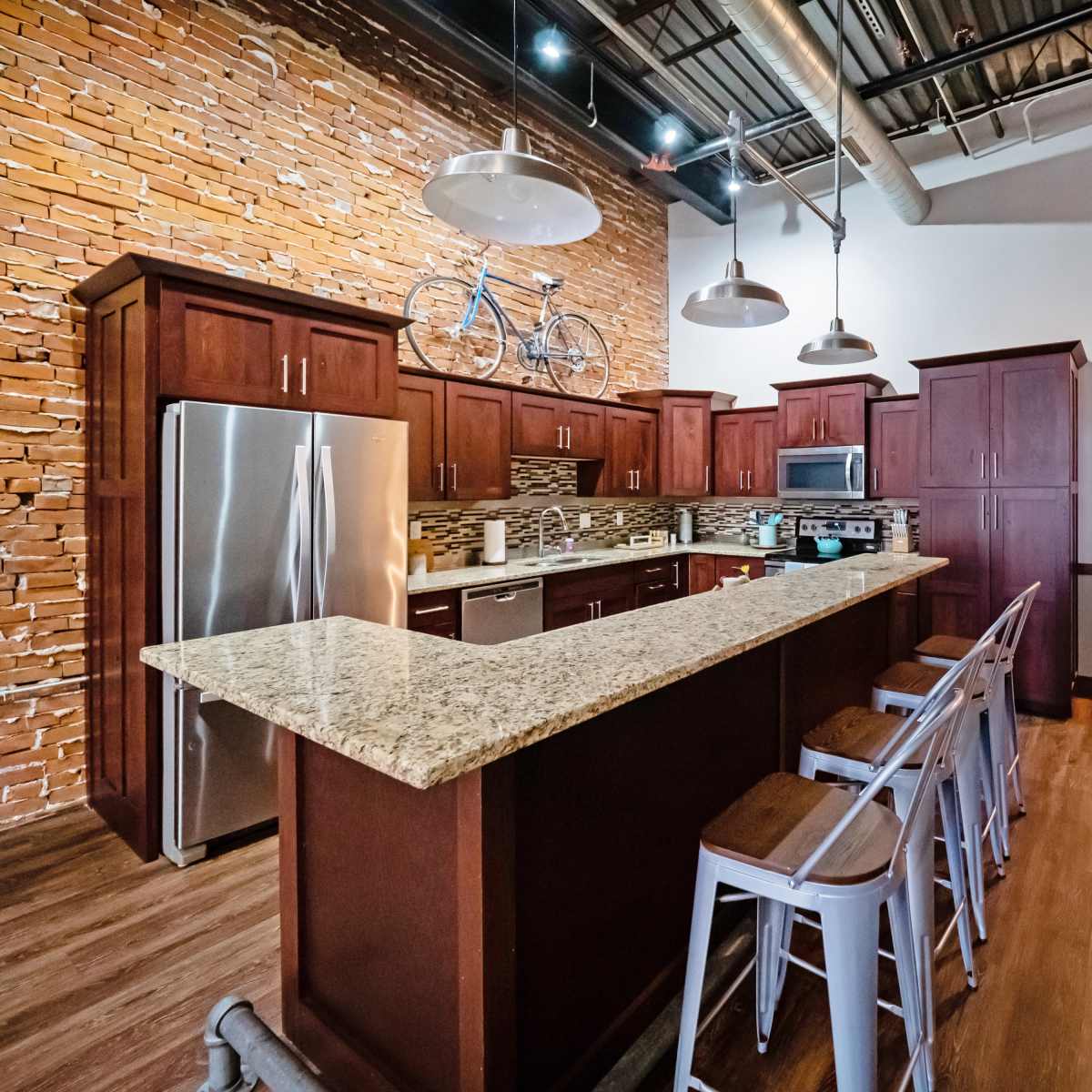 A modern kitchen featuring dark wooden cabinets, a granite countertop, and stainless steel appliances, with a bicycle mounted on the wall above.