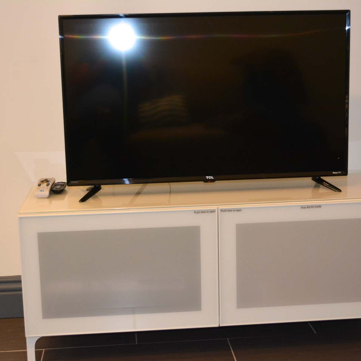 A black television is placed on a white media console with frosted glass doors and a remote control nearby.