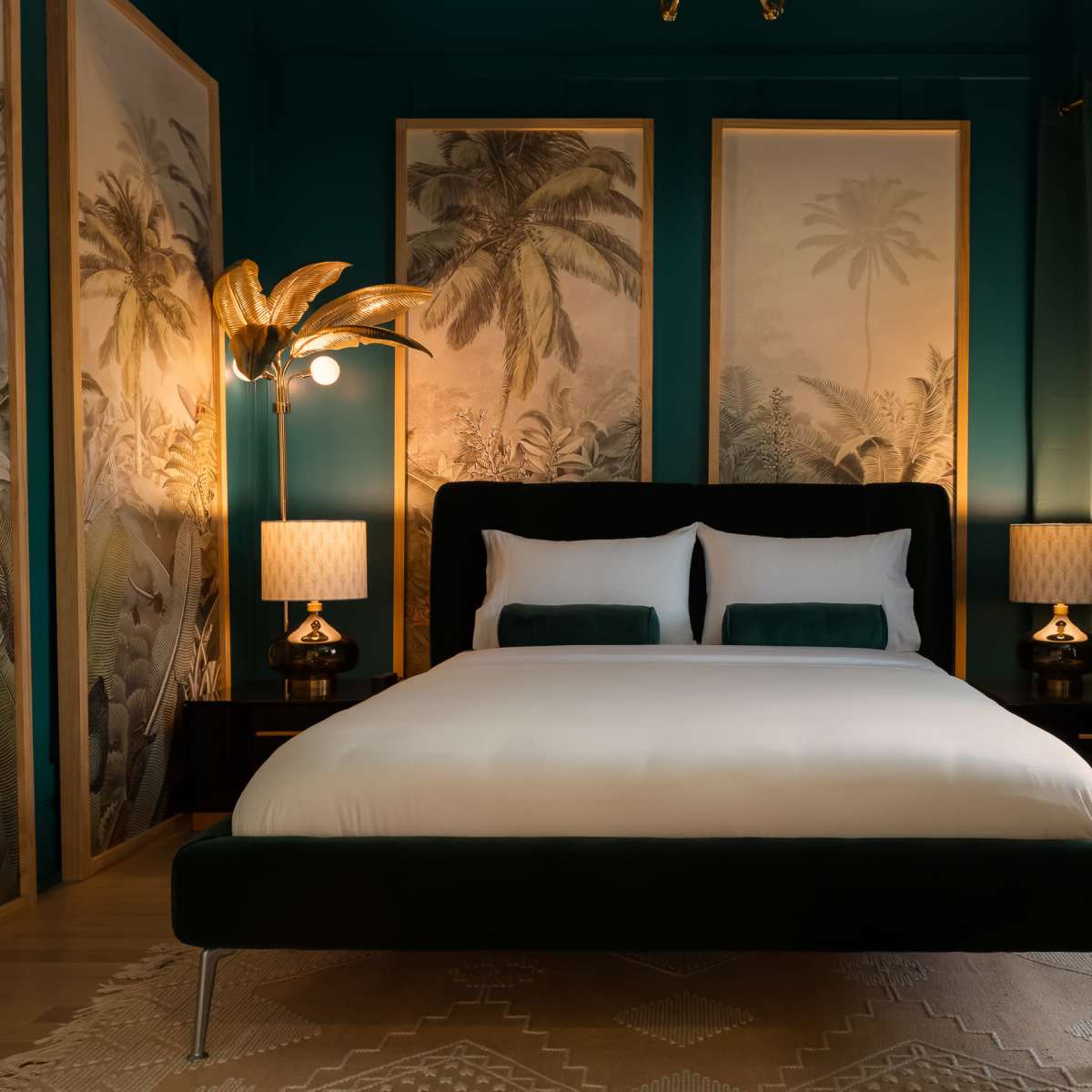 A stylish bedroom with a large bed, palm-themed artwork on the walls, and decorative lamps on either side.