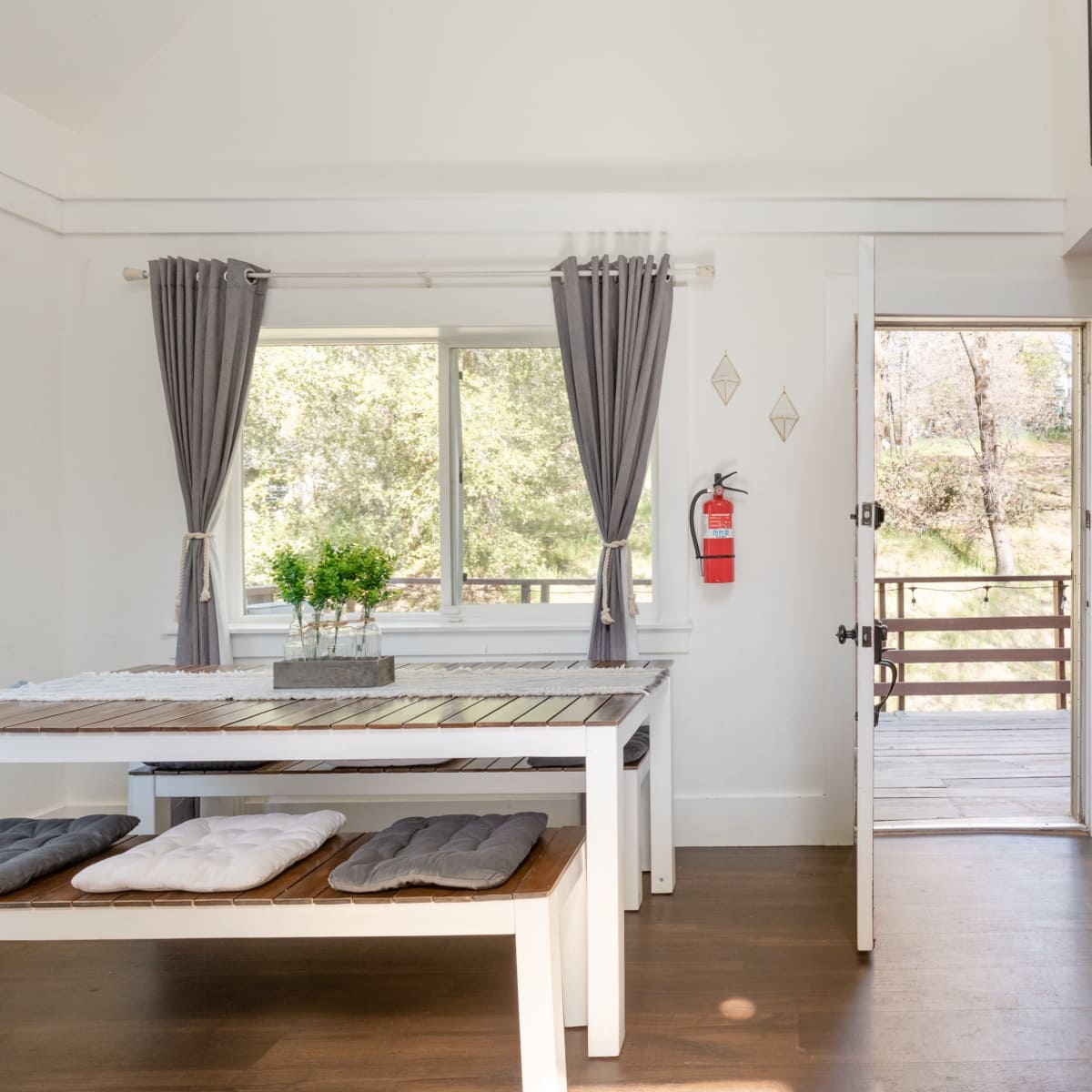 A spacious dining area features a long wooden table with bench seating and is connected to an outdoor deck through an open door.