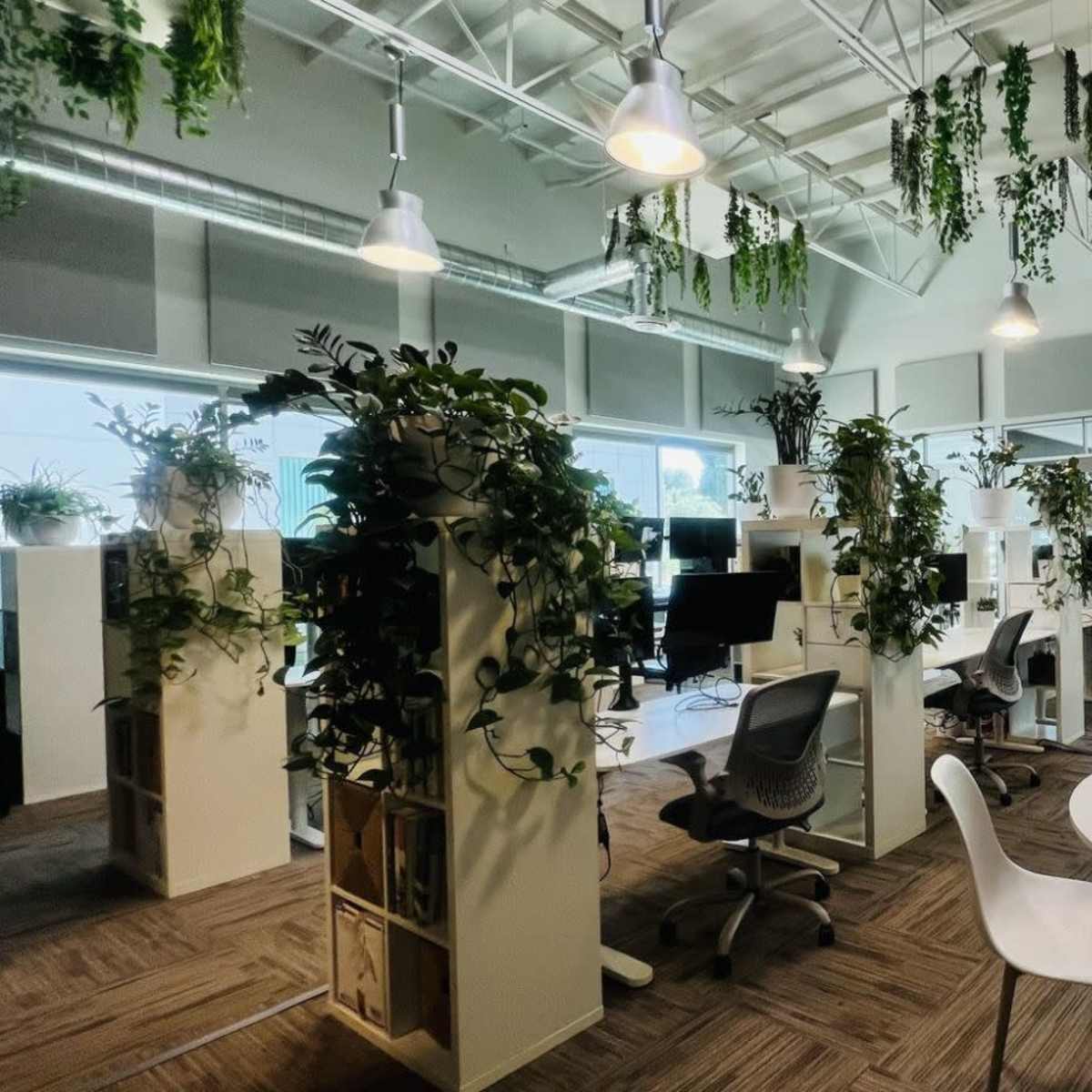 A modern office space with greenery, featuring workstations with computers and circular tables for collaboration.
