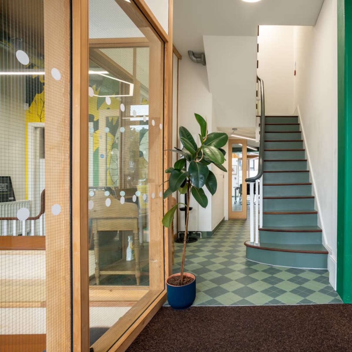 An interior hallway with a staircase leading to an upper level, flanked by a plant and a wall-mounted intercom system.