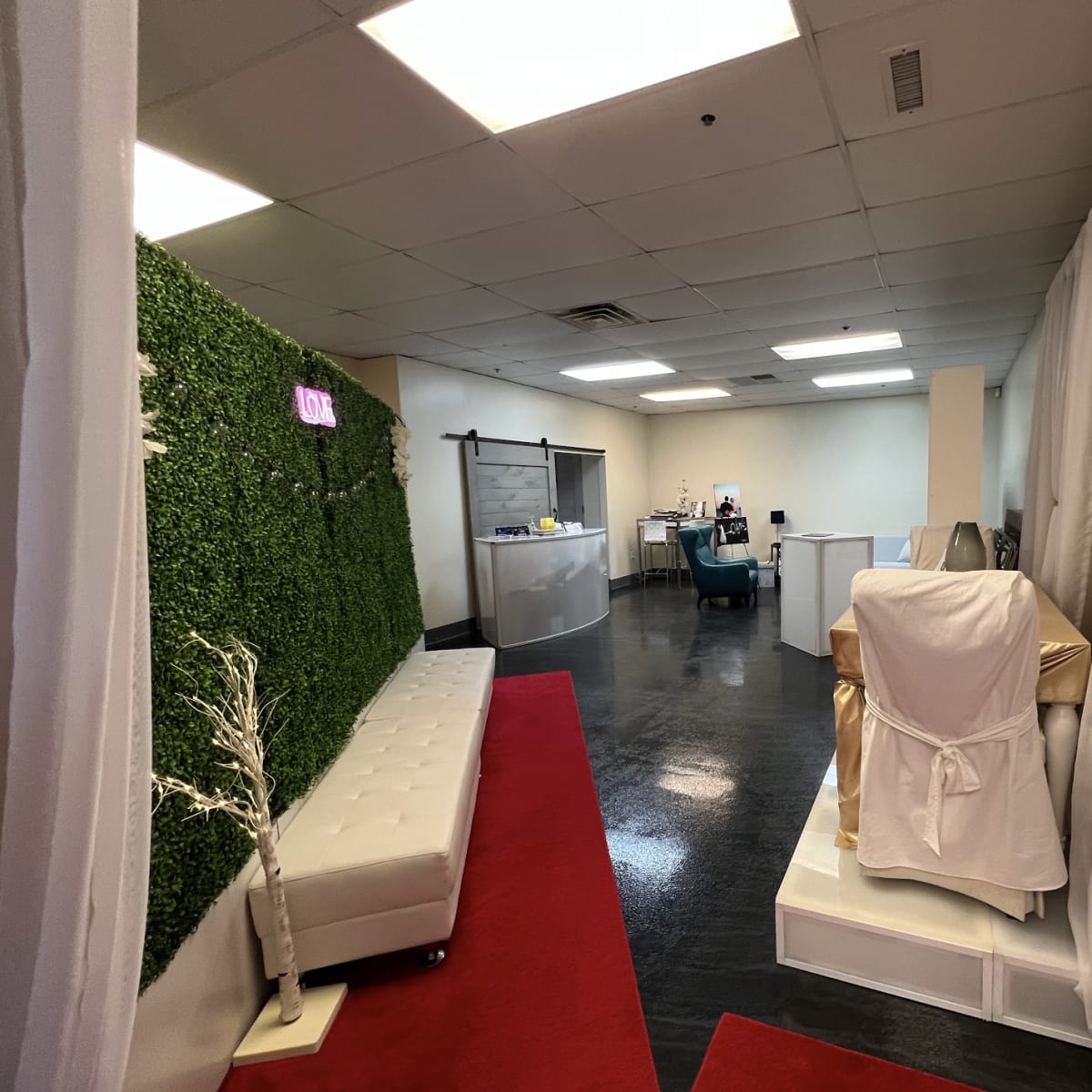 A spacious interior hallway leading to a reception area, with a green wall on one side and white drapes outlining a treatment room.