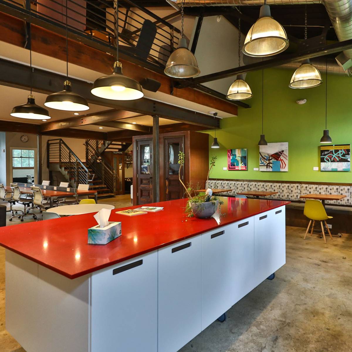 A modern open office space featuring a red kitchen island, green walls, various artworks, and a mix of seating areas.