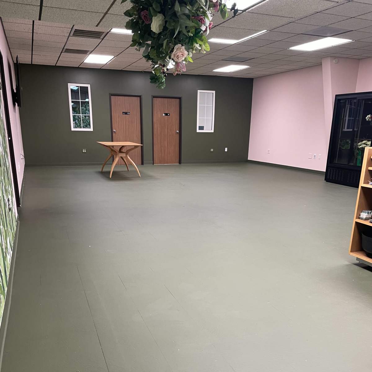An empty room with green and pink walls, a wooden table in the center, and two doors at the far end.