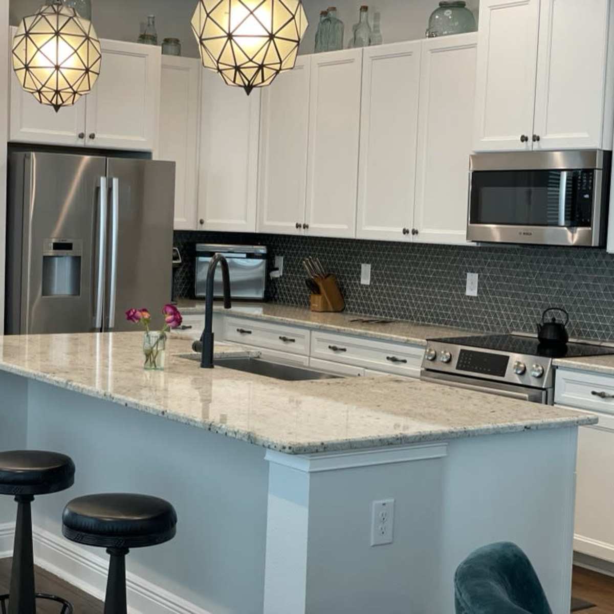 A modern kitchen with white cabinets, a marble countertop, and two pendant lights hanging above the island.