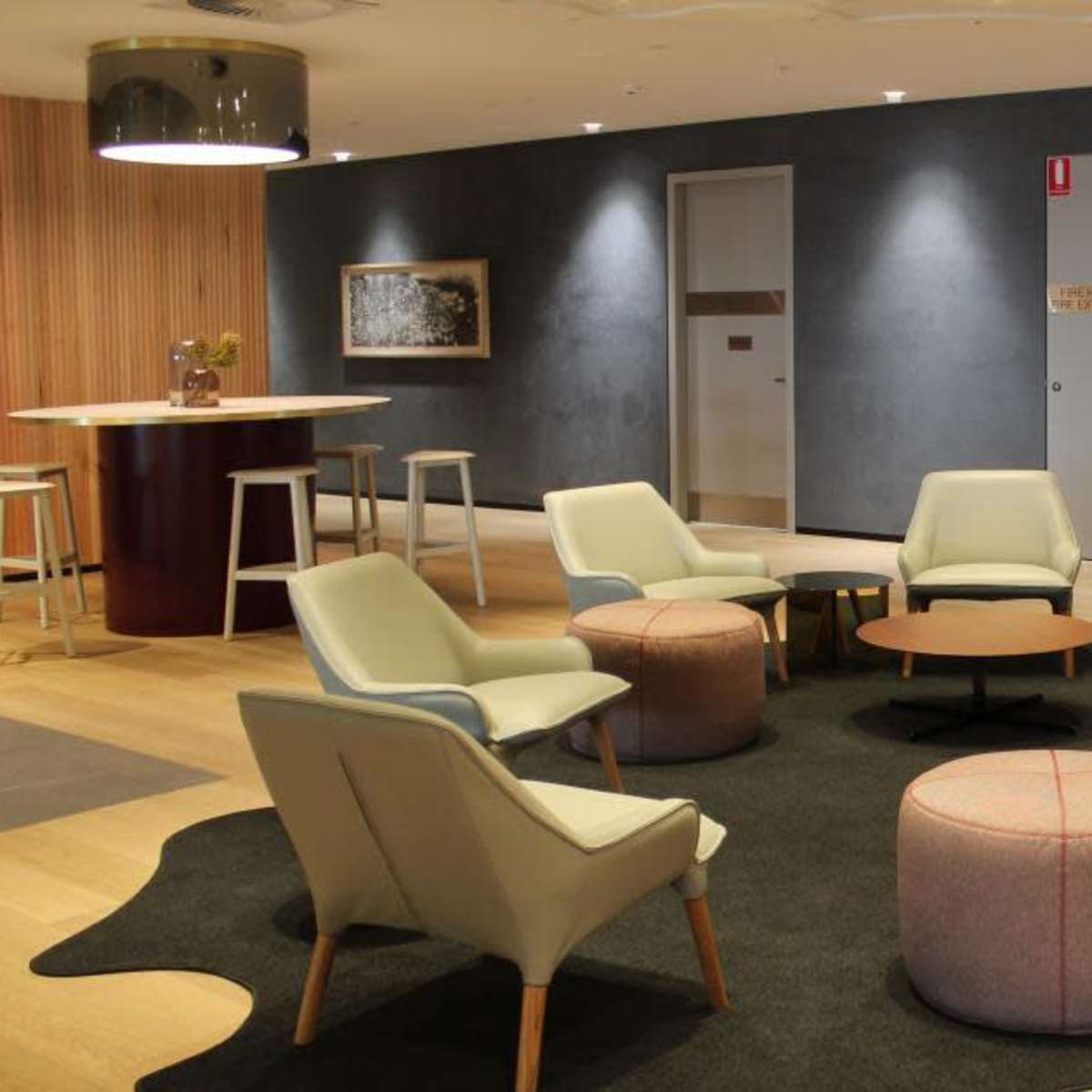 A modern lounge area with four light-colored chairs, two gray poufs, and a round coffee table set on a dark rug.