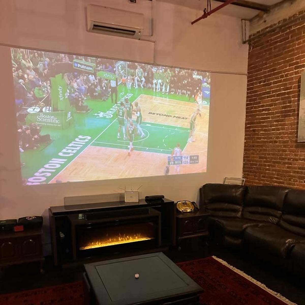 A basketball game is being projected onto a wall in a room featuring a leather couch and a low coffee table.