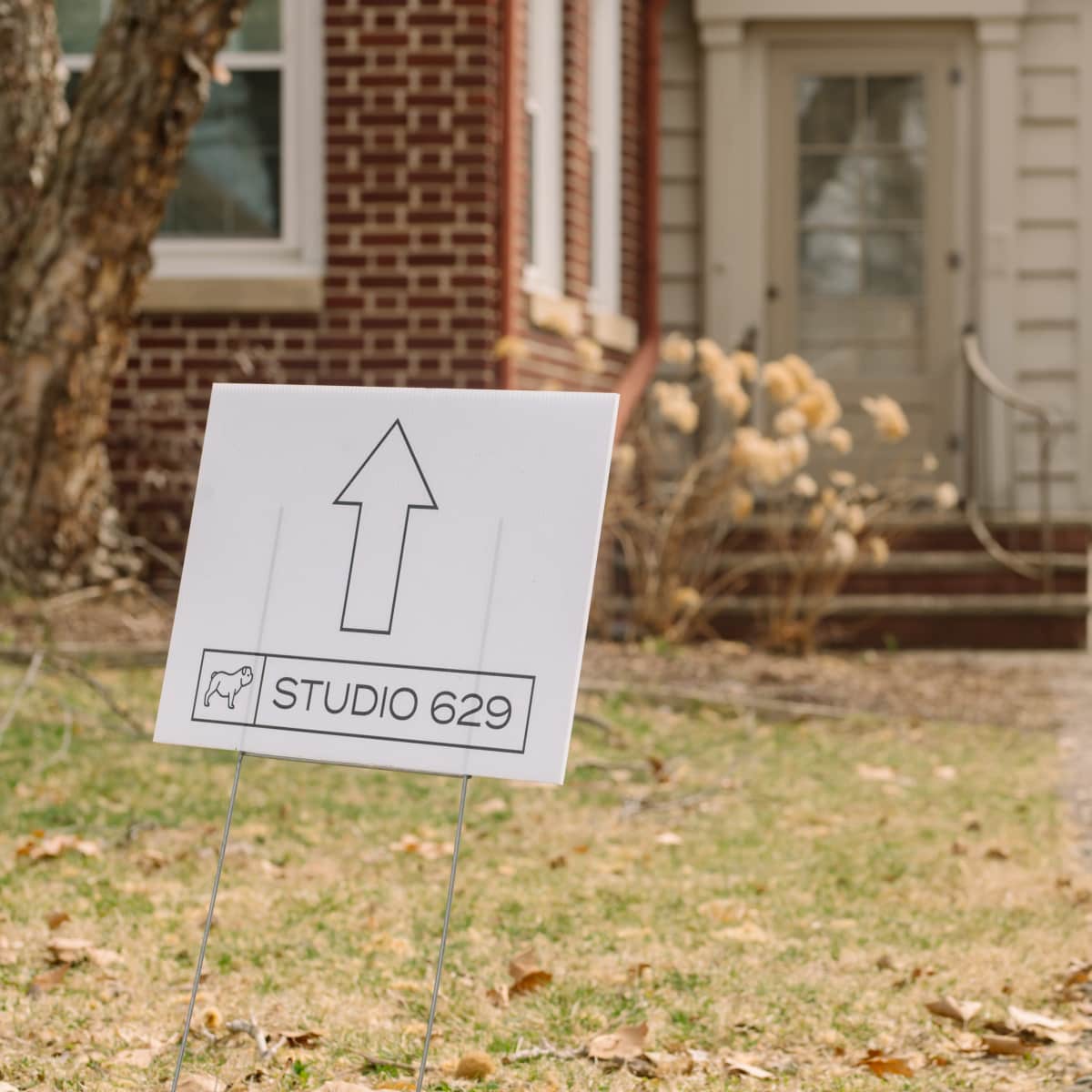 A directional sign labeled "STUDIO 629" is placed in the yard, guiding visitors toward the entrance of a brick house.