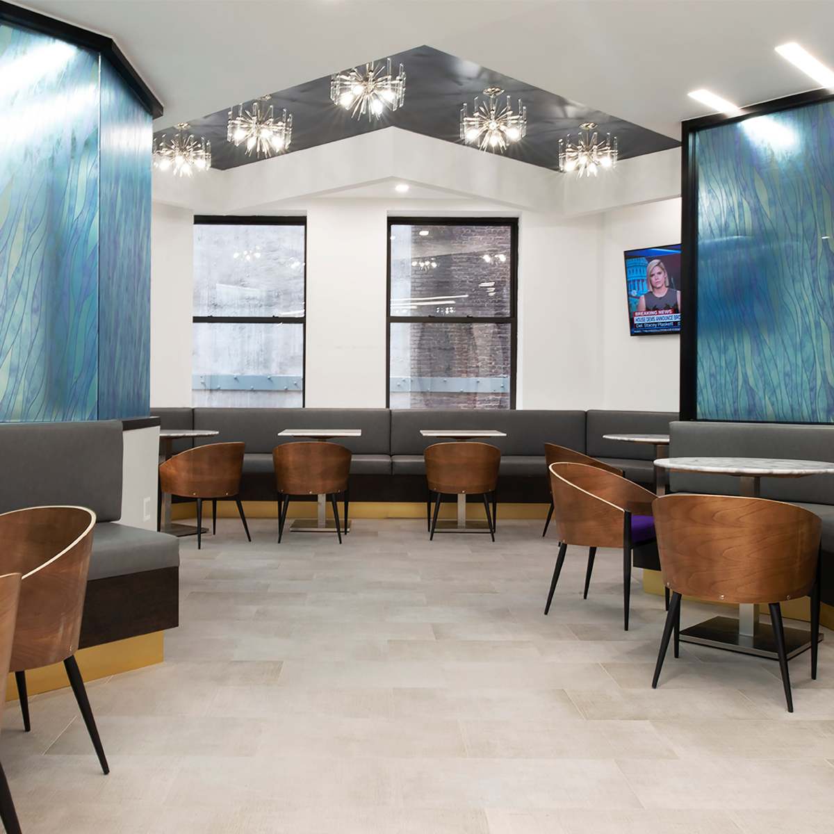 A modern lounge area with gray seating, wooden chairs, and walls featuring a blue and green abstract design, illuminated by decorative light fixtures.
