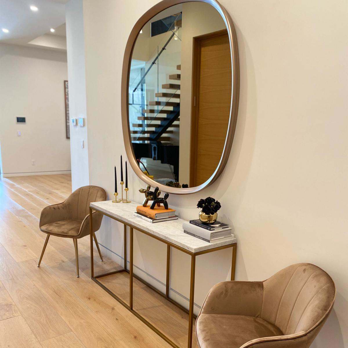 A hallway featuring a circular mirror above a marble-top console table flanked by two upholstered chairs and decorative items.