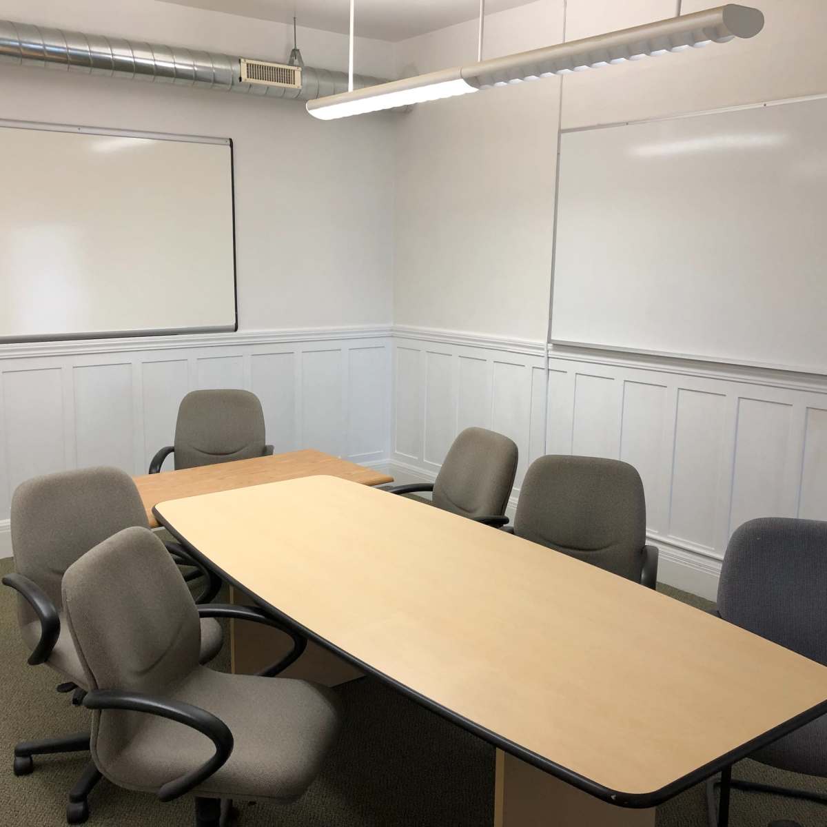 A small meeting room features an oval table surrounded by chairs, with two whiteboards on the walls.