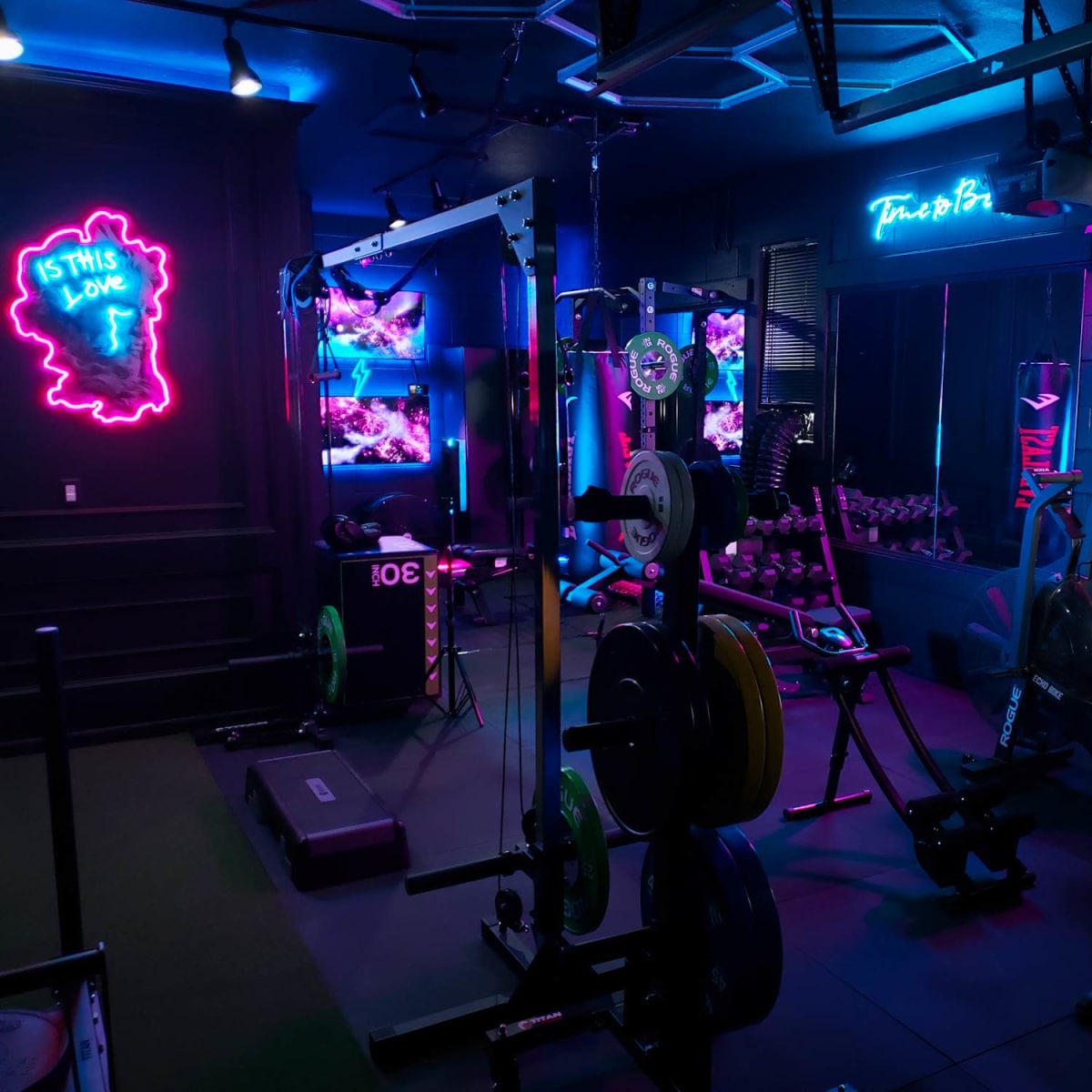 A dimly lit gym featuring various weightlifting equipment, neon signs, and vibrant wall art.